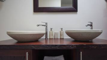 A bathroom with two large, beige, bowl-shaped sinks, a dark wooden countertop, a mirror above the sinks, and a towel hanging in a cabinet below.