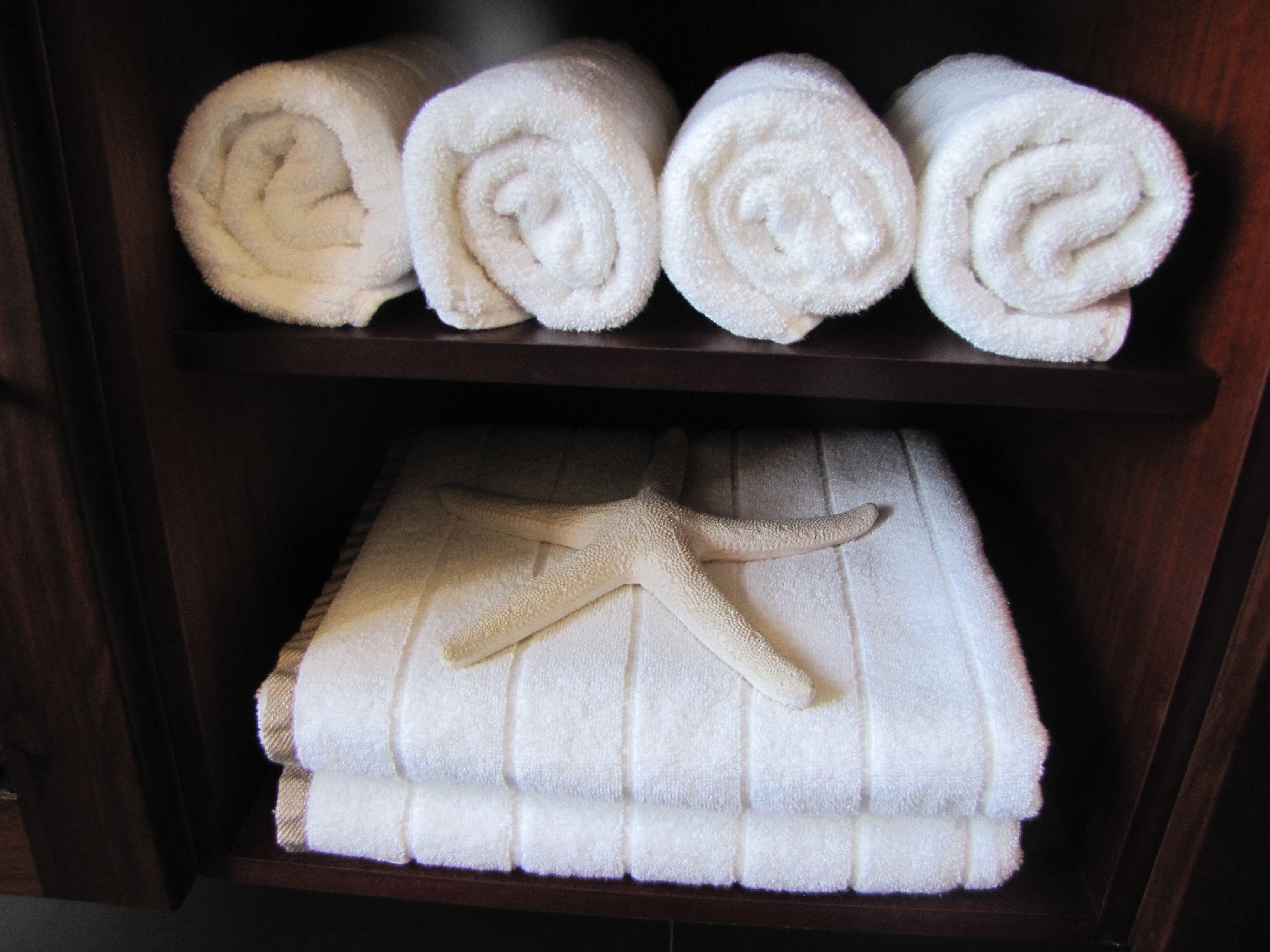A shelf with four rolled white towels and a folded towel with a starfish design.