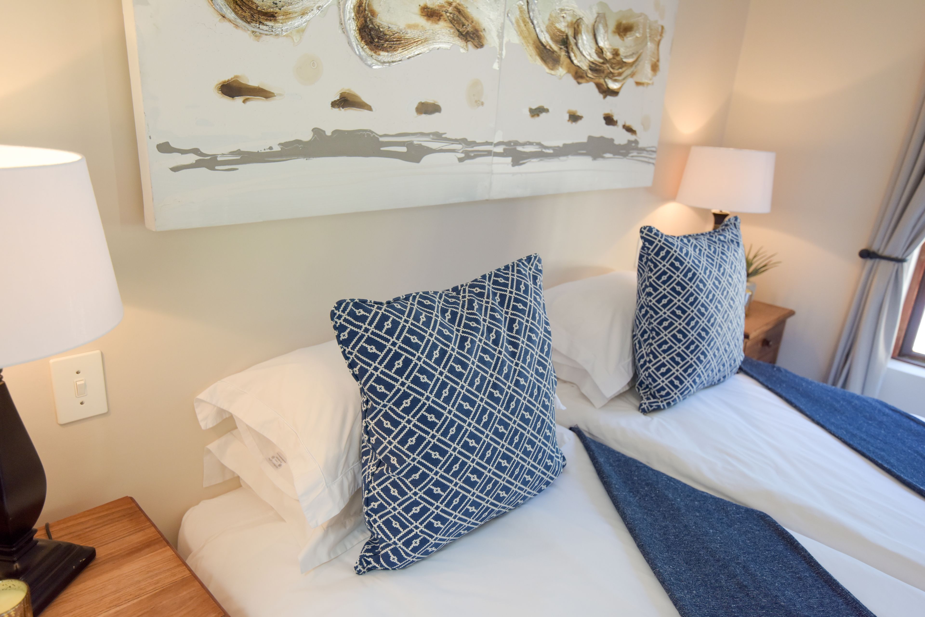 A hotel room with a bed, two patterned pillows, a bedside lamp, a nightstand, and a wall art piece.