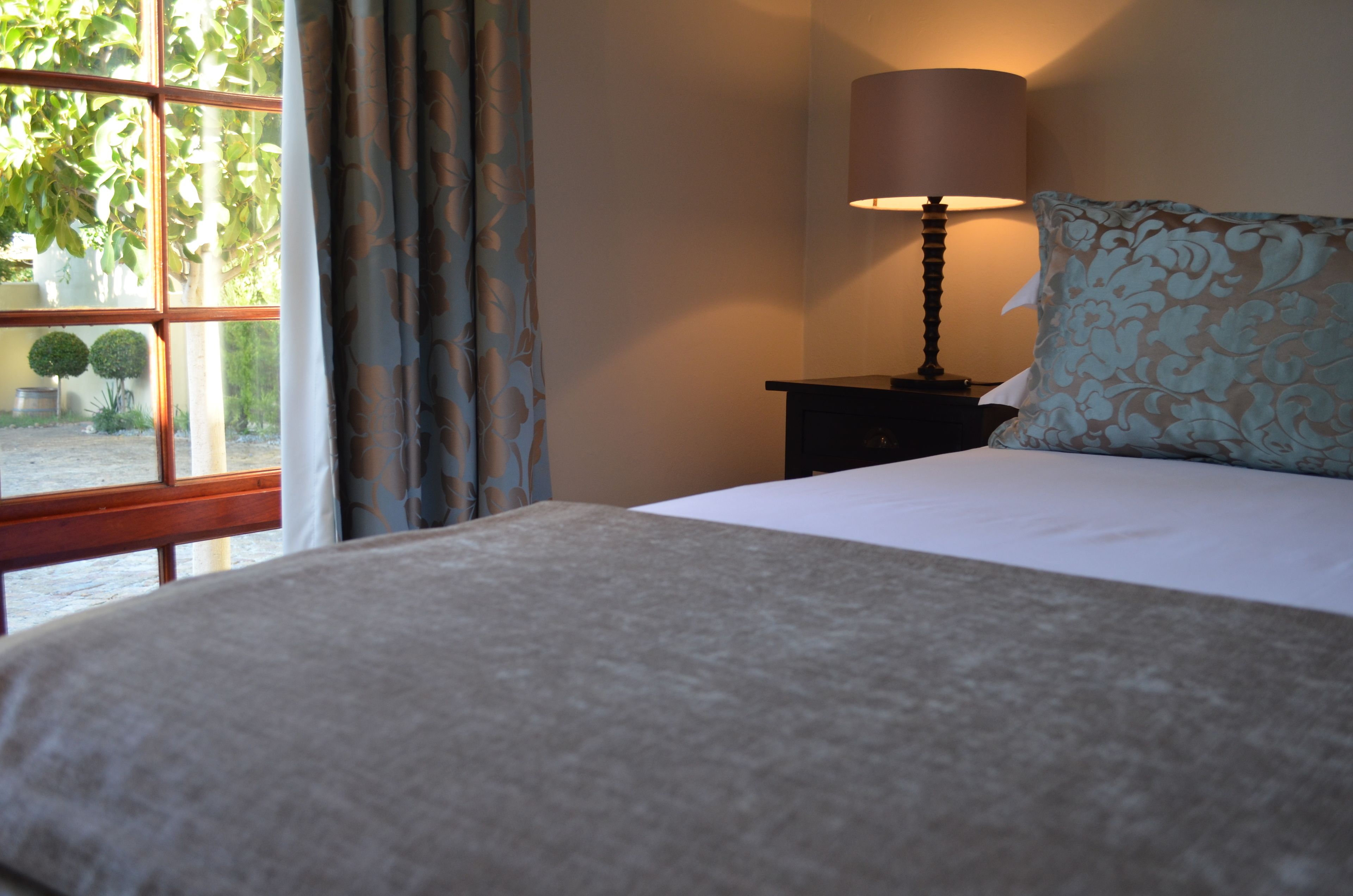 A neatly made bed with a white duvet, a lamp on a bedside table, and a window with curtains.