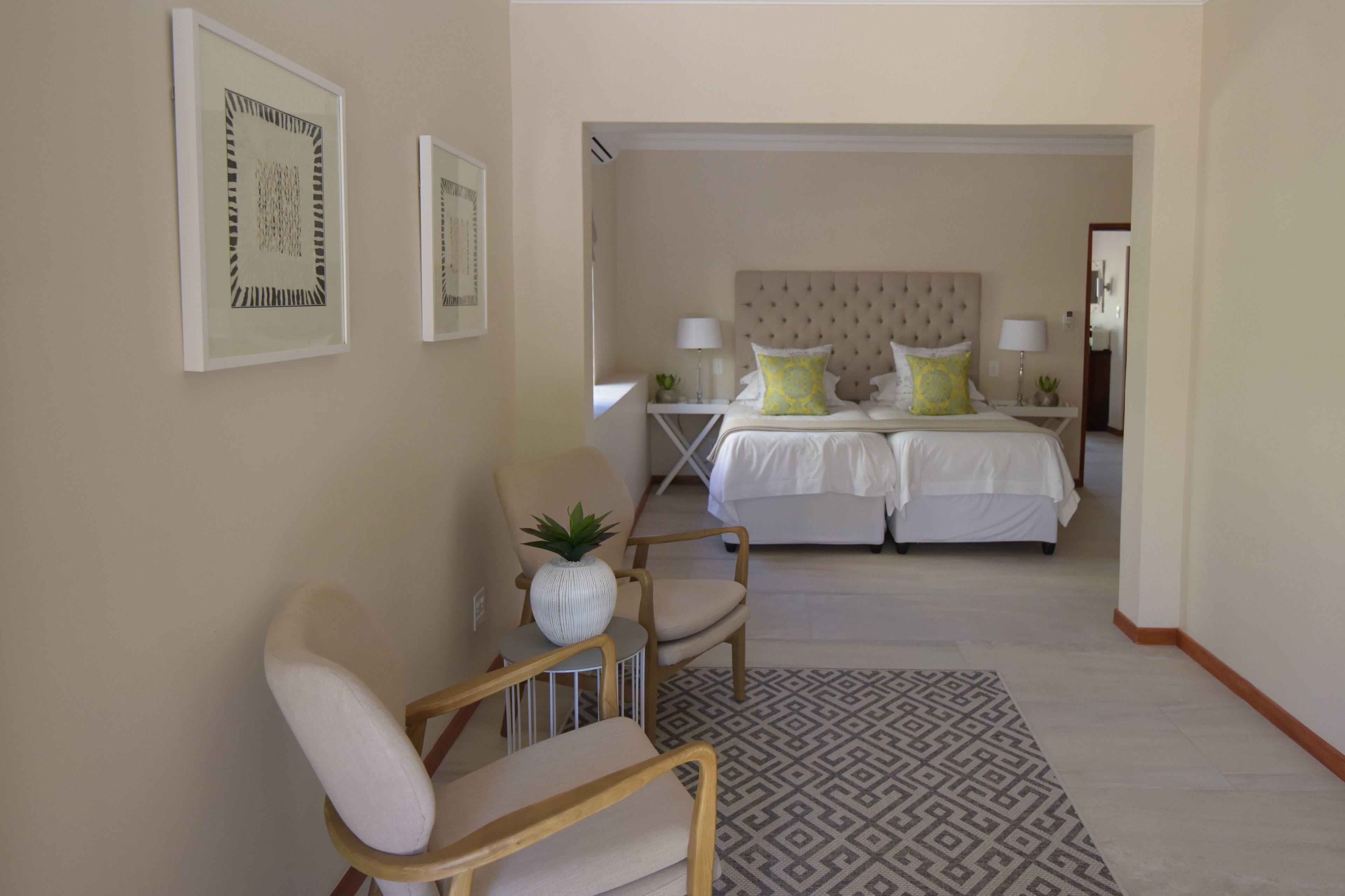 A hotel room with a bed, two bedside tables, a chair, a patterned rug, and two framed artworks on the wall.