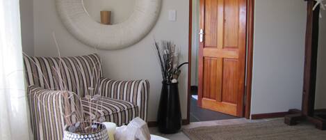 A living room with a striped sofa, a round mirror, a vase with dried plants, and a wooden door.