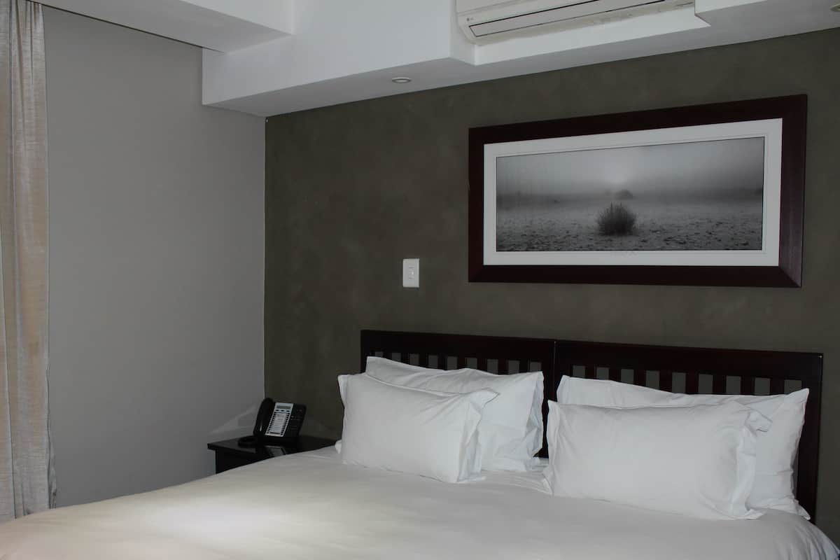 Habitació d'hotel amb un llit, una taula de nit amb un telèfon, un quadre al mur i una finestra amb cortines.