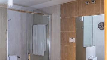 Un baño moderno con cabina de ducha de vidrio, tocador color beige con lavamanos y un espejo grande.