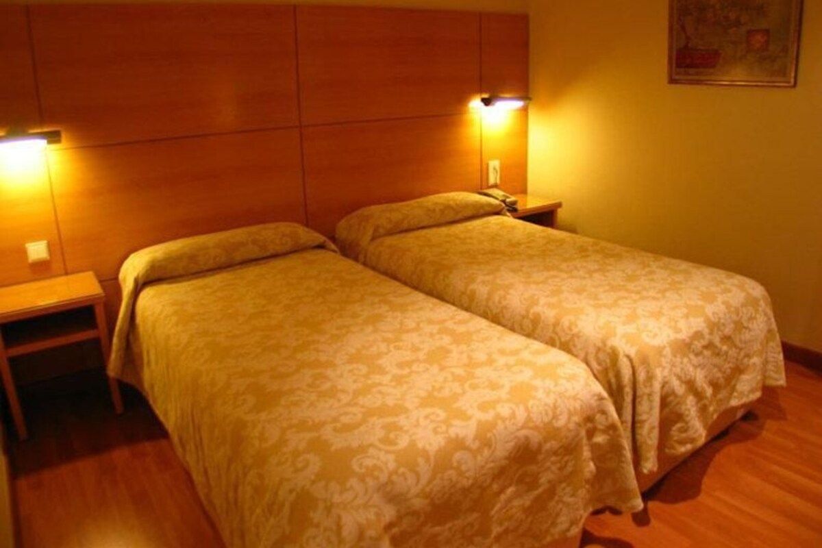 A hotel room with two single beds, wooden headboard, bedside lamps, and a small table.