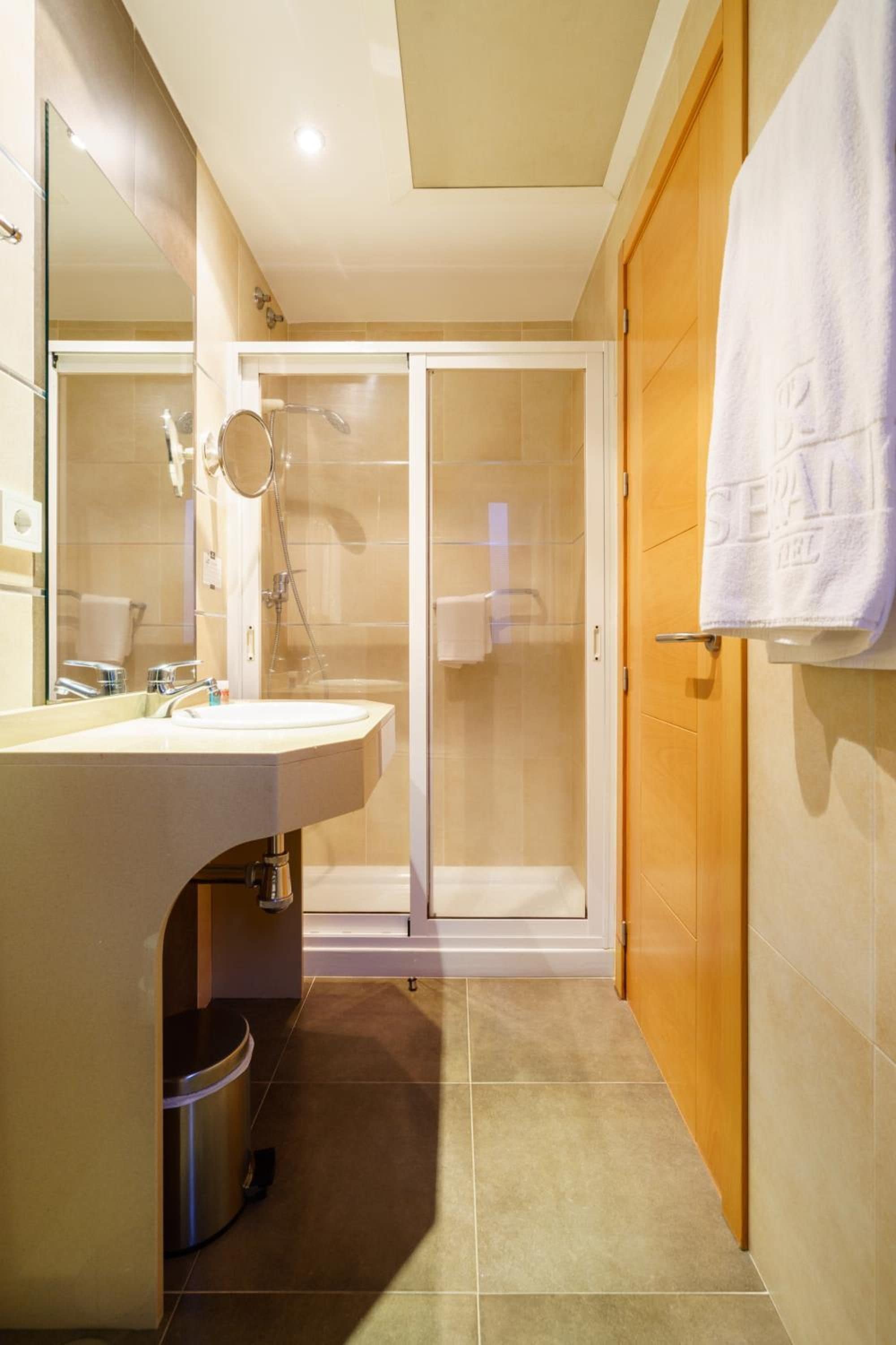 A modern bathroom with a sink, mirror, shower, and a towel hanging on the wall.
