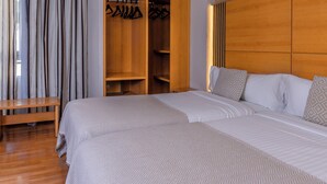 A hotel room with two beds, a wooden wardrobe, and a bench.