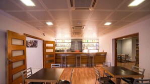 A conference room with a long table, chairs, a bar area with shelves of bottles, and a wooden door with frosted glass panels.