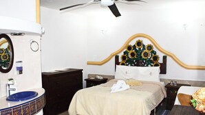 A bedroom with a bed, a bedside table, a nightstand, a mirror, a ceiling fan, and a bathroom with a sink and toilet. - Hotel El Refugio (Tlaxcala)