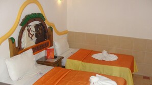 A hotel room with two single beds, each with an orange bedspread and a white towel folded on top. There is a wooden headboard with a decorative design, and a small bedside table with a book and a red card. - Hotel El Refugio (Tlaxcala)