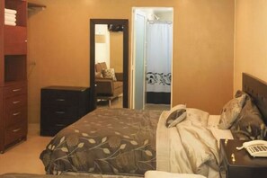 Une chambre à coucher avec un lit, une commode, un miroir et une salle de bain visible à travers une porte ouverte.