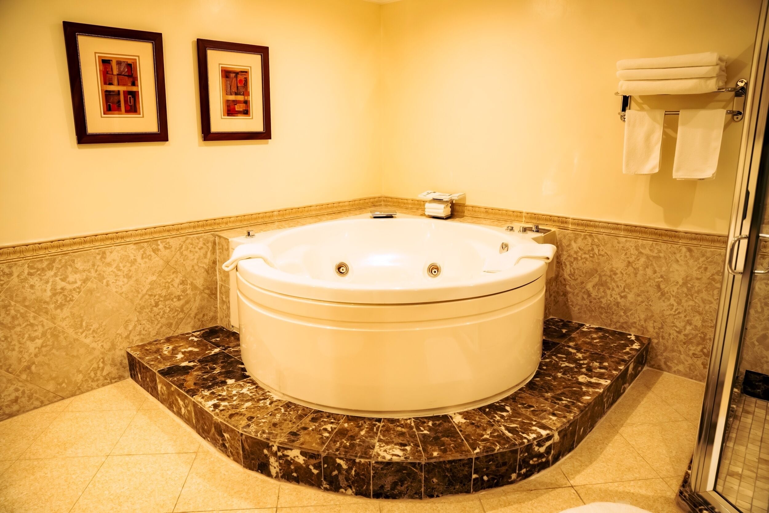 A bathroom with a large bathtub, a shower, and two framed pictures on the wall.