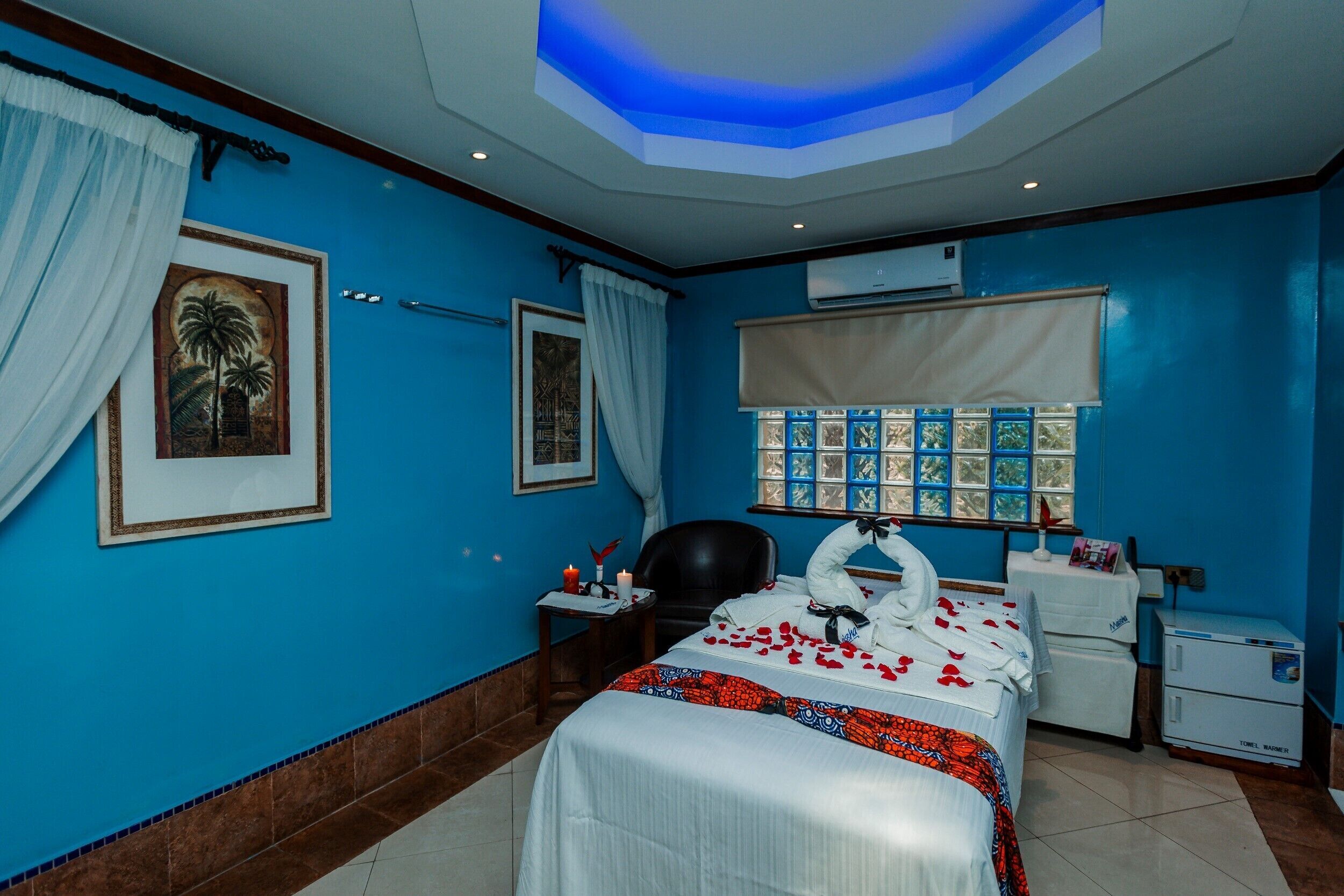 A hotel room with a bed, a desk, a chair, a window with a view, and an air conditioning unit.