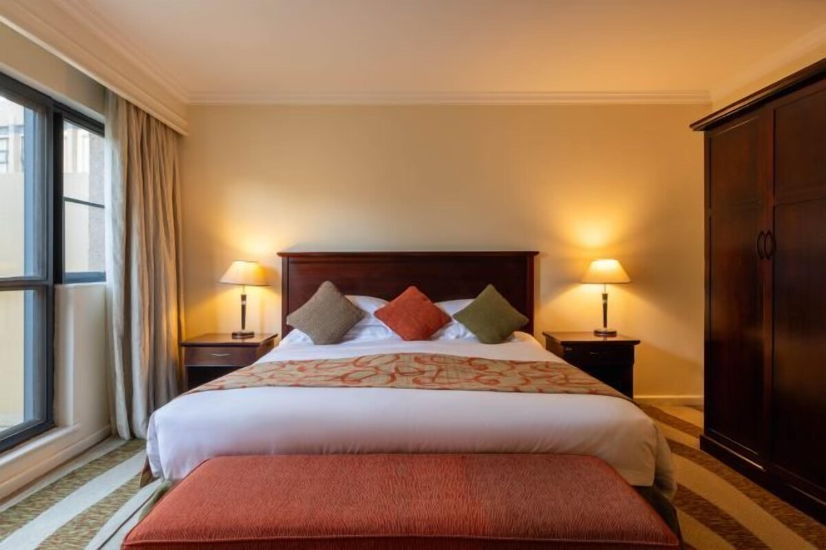 Habitación de hotel con una cama grande, dos lámparas de noche, un armario y una ventana con cortinas.