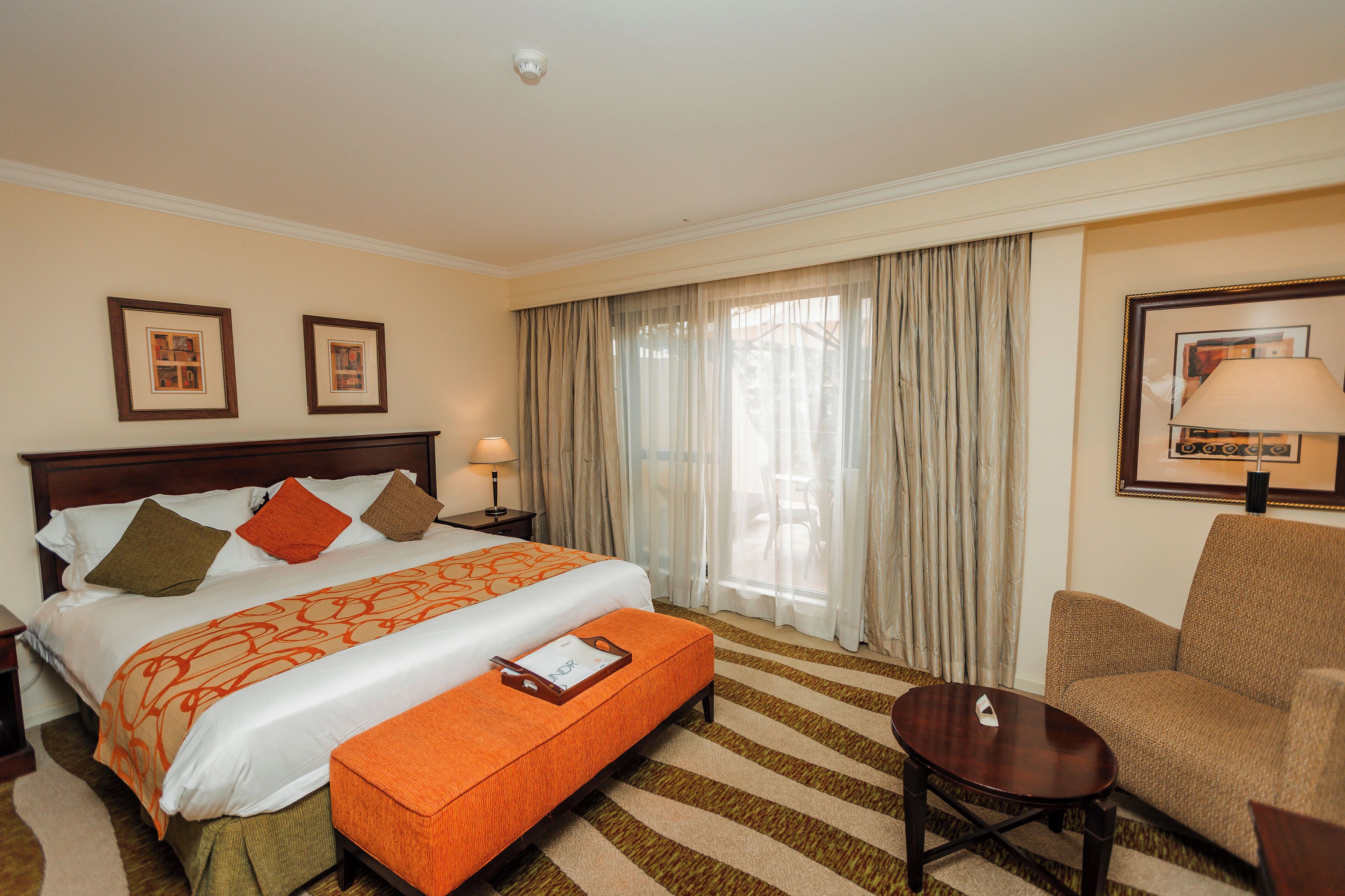 Habitación de hotel con cama, mesita de noche, una silla, escritorio y ventana con cortinas.