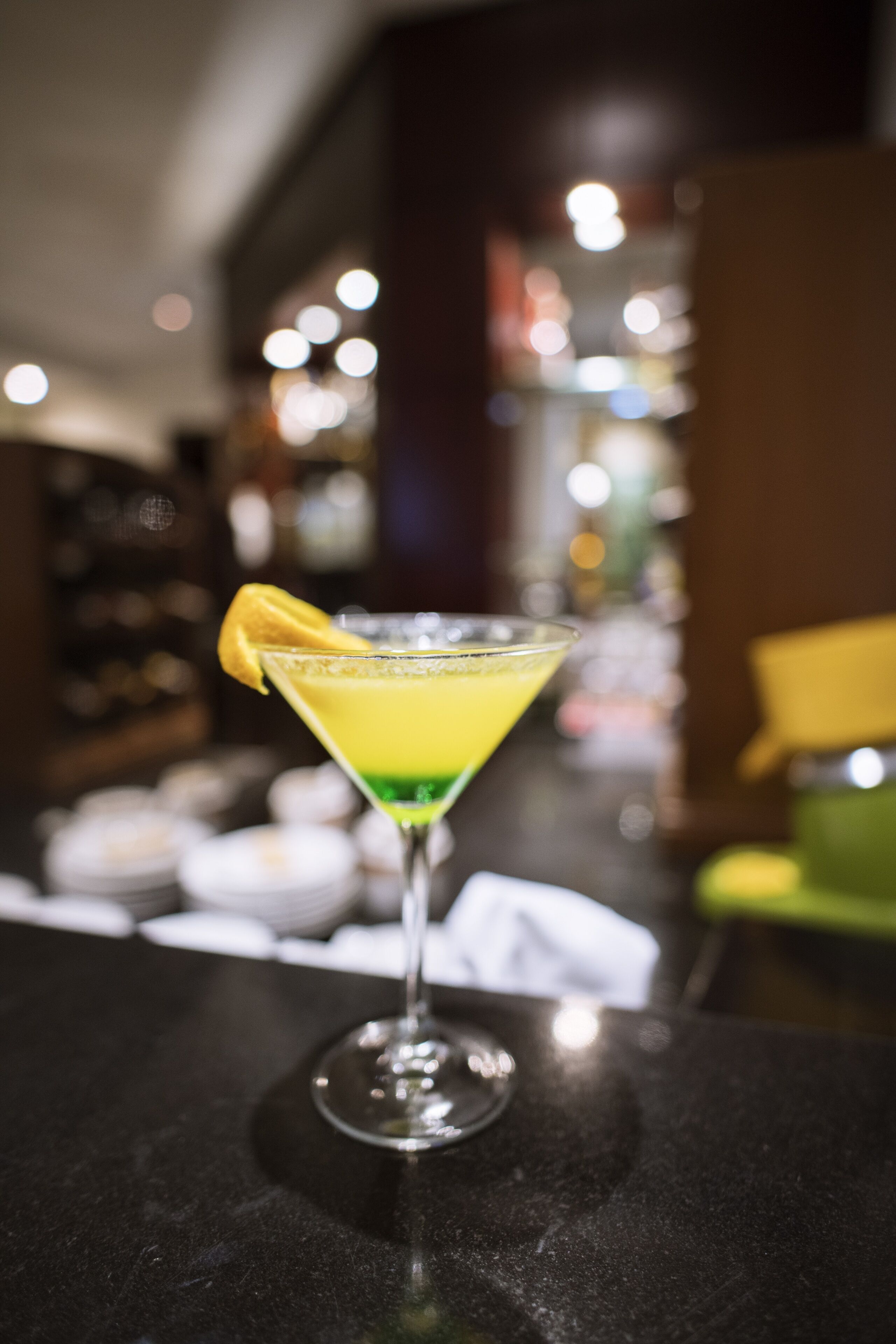 Un cocktail servi dans un verre à martini, décoré d’une tranche de citron, posé sur le comptoir d’un bar.