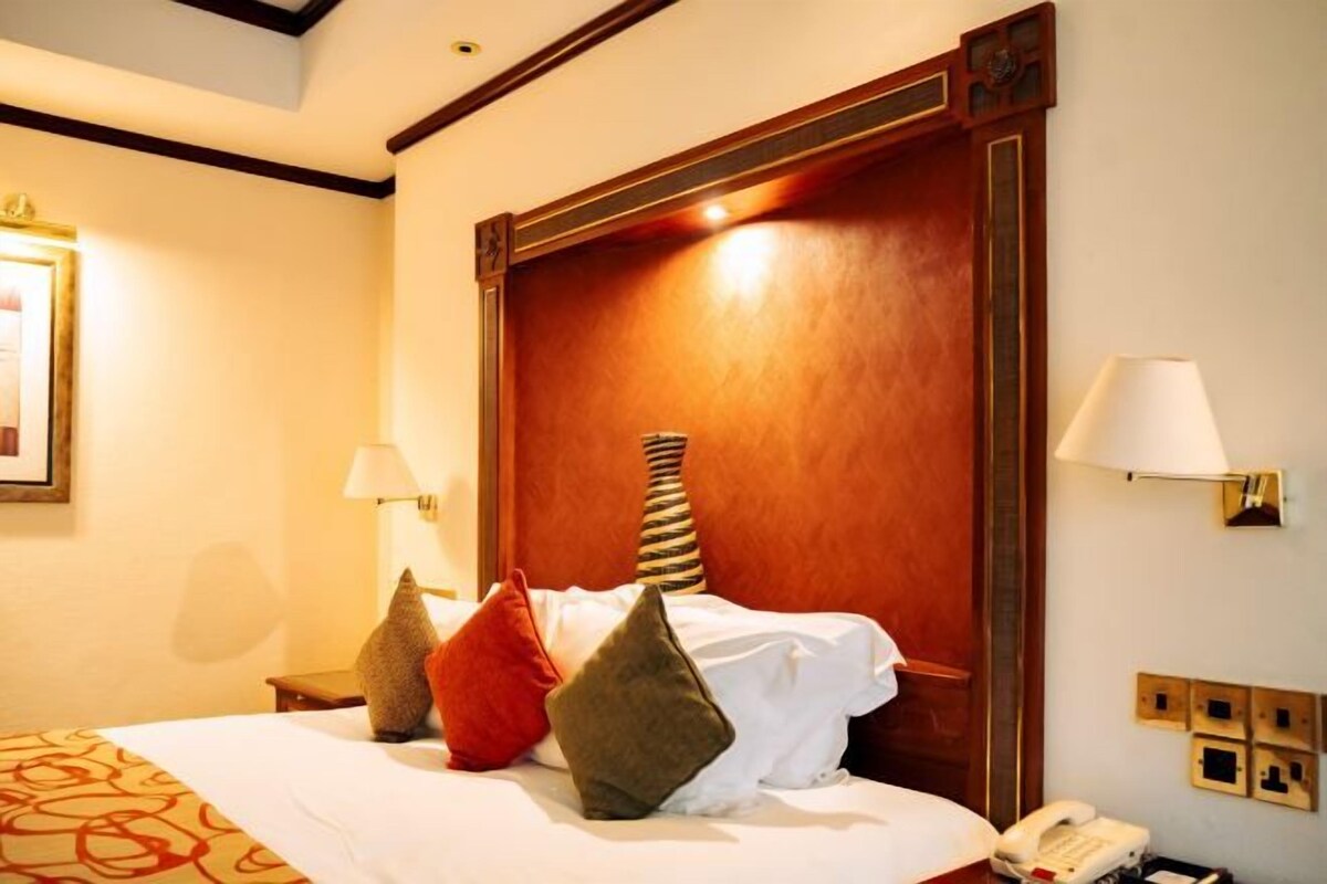 A hotel room with a large bed, bedside lamps, a telephone, and a wall-mounted light fixture.