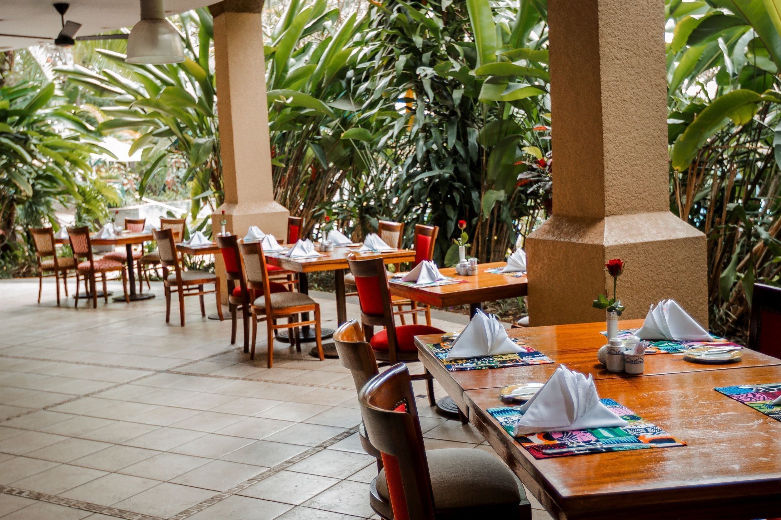 A restaurant with wooden tables and chairs, surrounded by lush green plants.