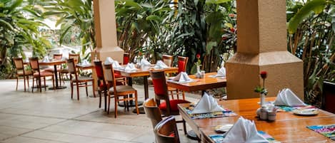Un restaurante con mesas y sillas de madera, rodeado de exuberante follaje.