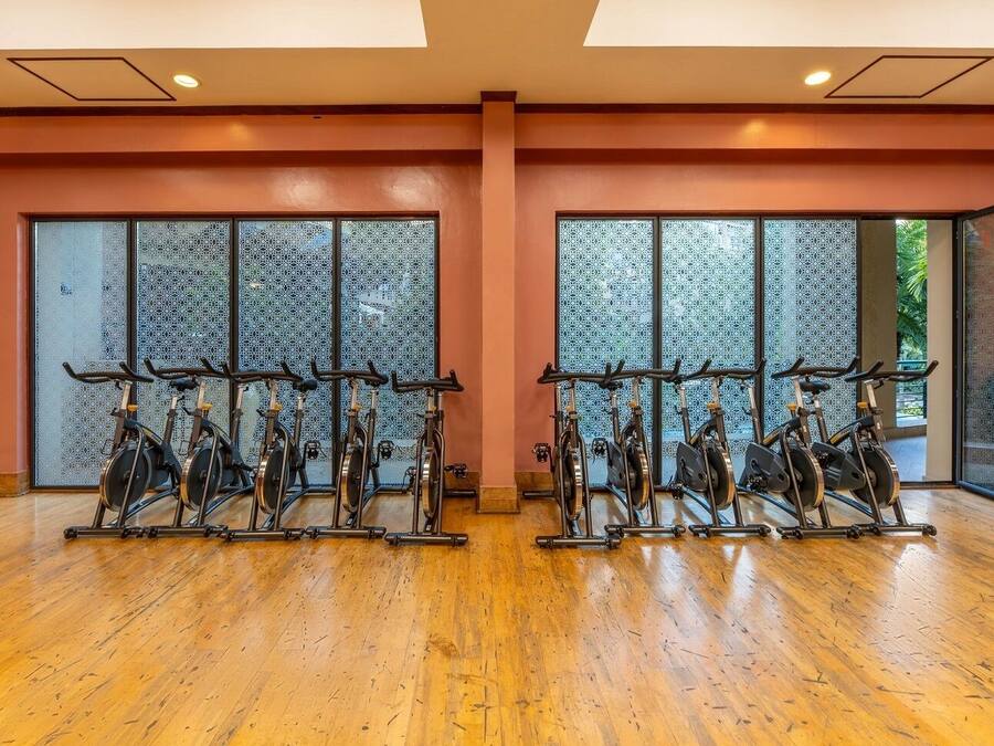 Una palestra con cyclette e macchinari cardio, ampie finestre con vetri decorati e un pavimento in legno.