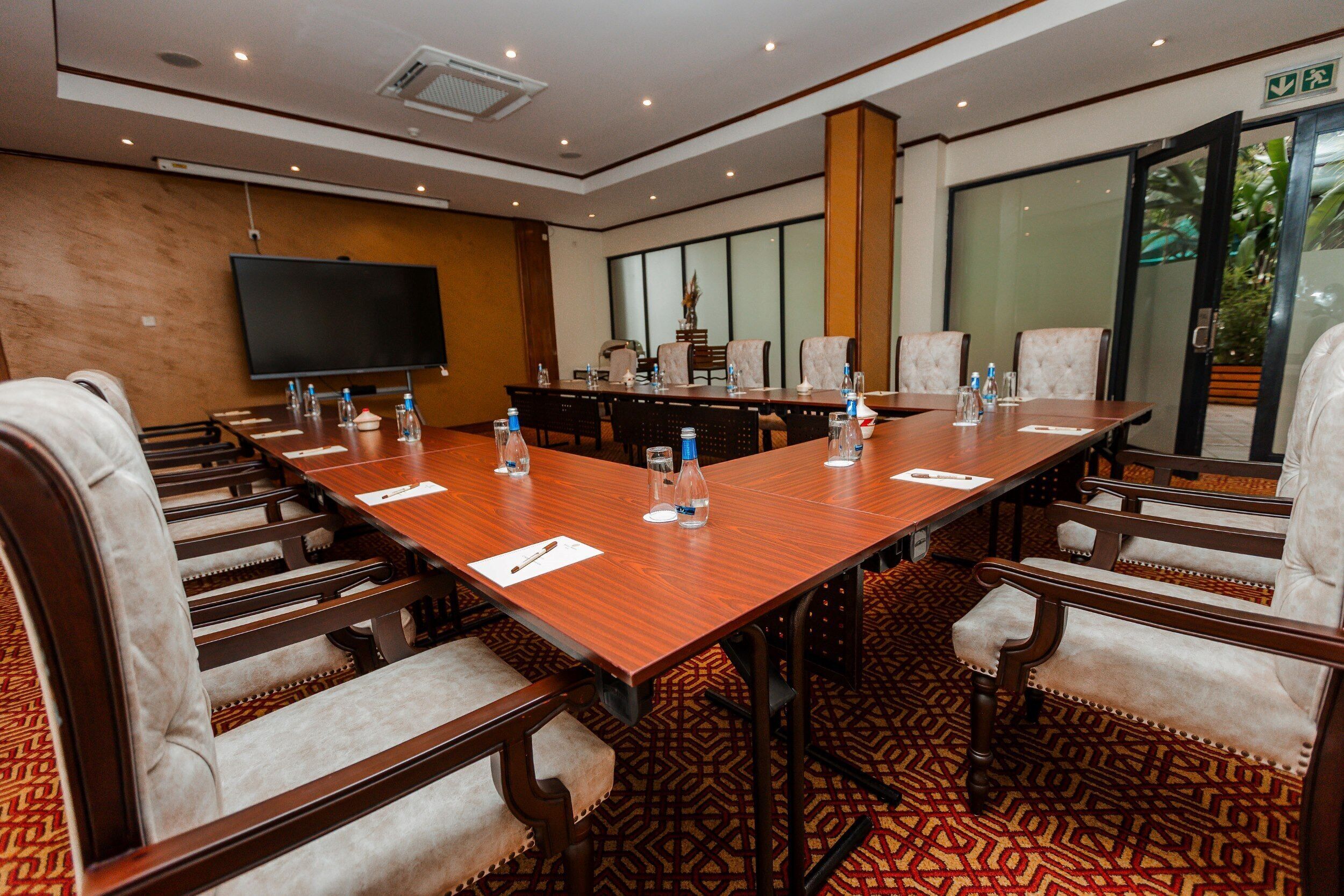 A conference room with a long table, chairs, a flat-screen TV, and a patterned carpet.