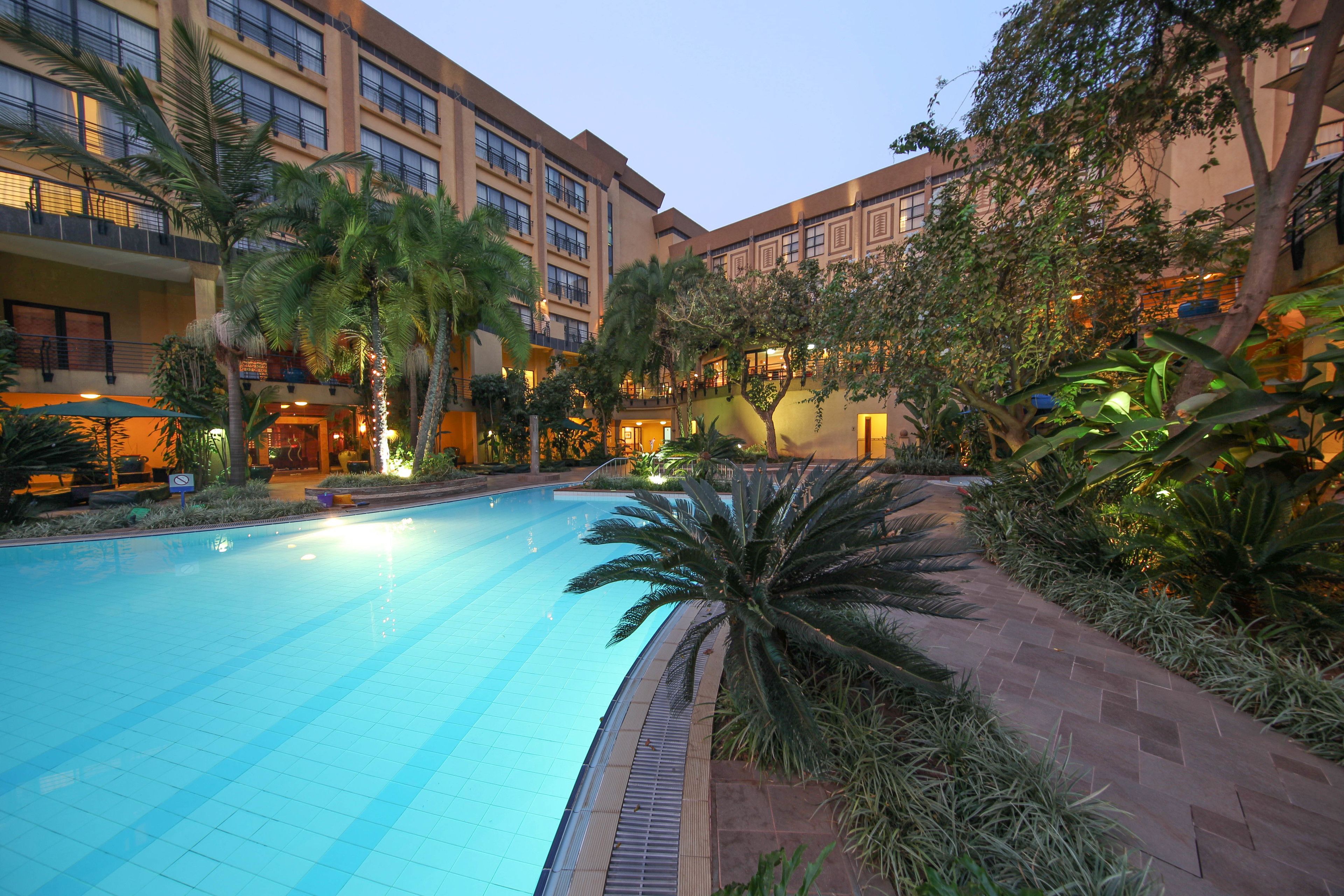A hotel courtyard with a swimming pool, palm trees, and a brick pathway.