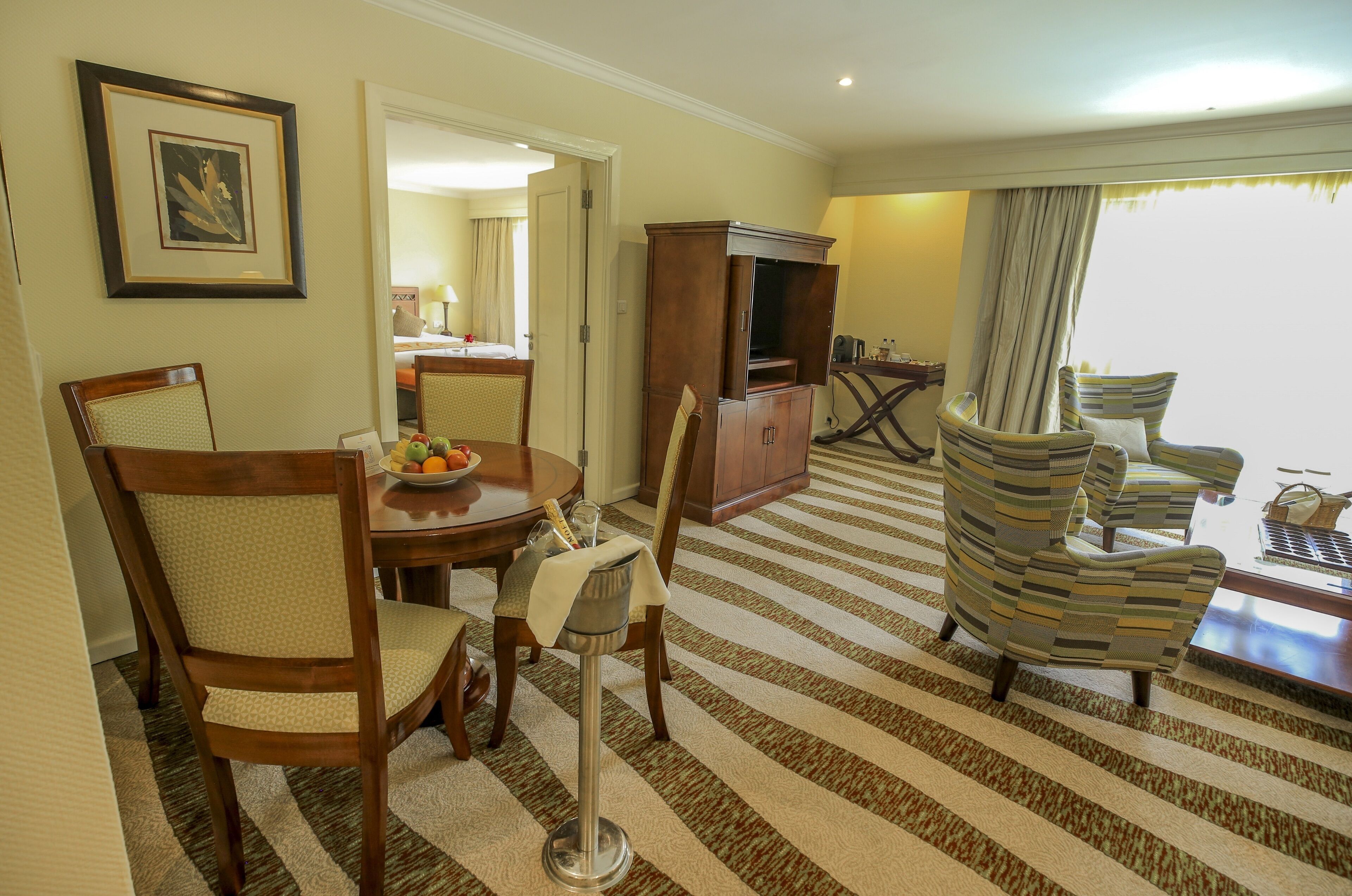 A hotel room with a dining table, chairs, a TV stand, and a striped carpet.