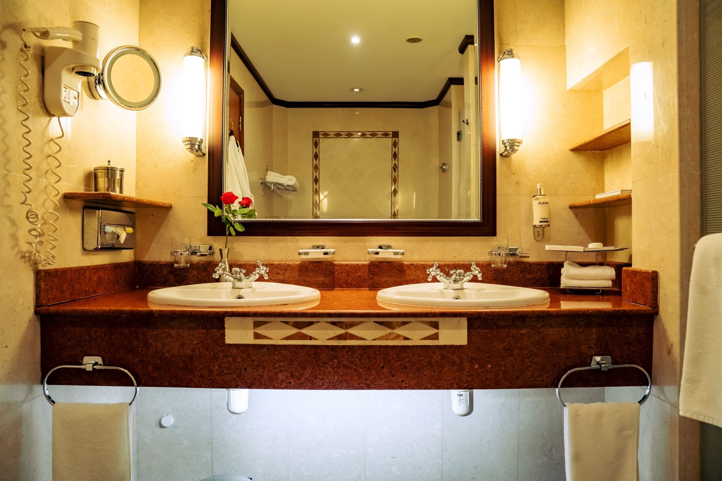 Un baño de hotel con dos lavamanos, un espejo, un secador de pelo y un perchero para toallas.