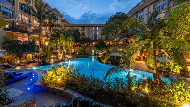 A hotel courtyard with a swimming pool, palm trees, and outdoor seating areas. - Kigali Serena Hotel (Kigali)