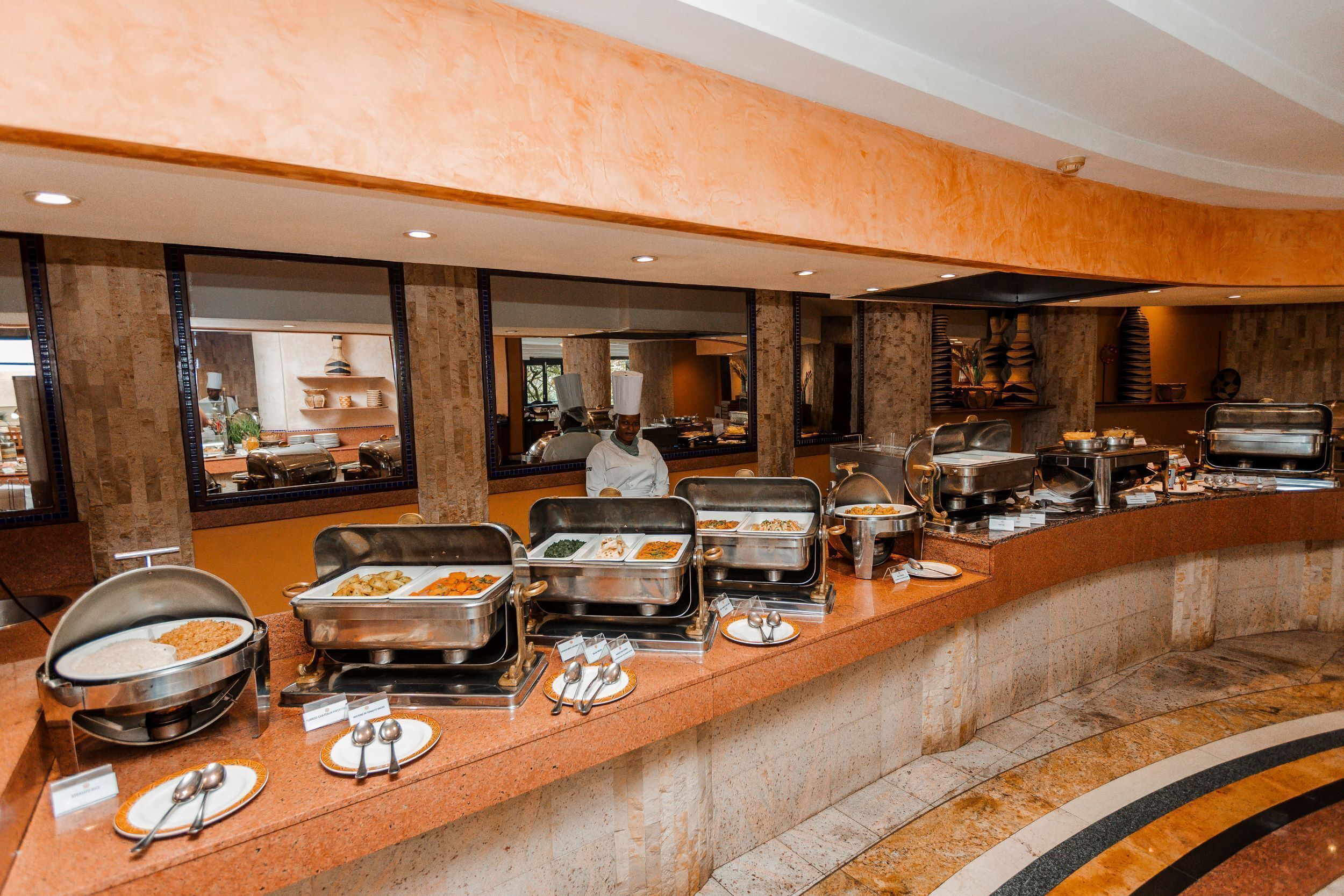 A buffet setup with various food stations, a chef in uniform, and a modern interior design.