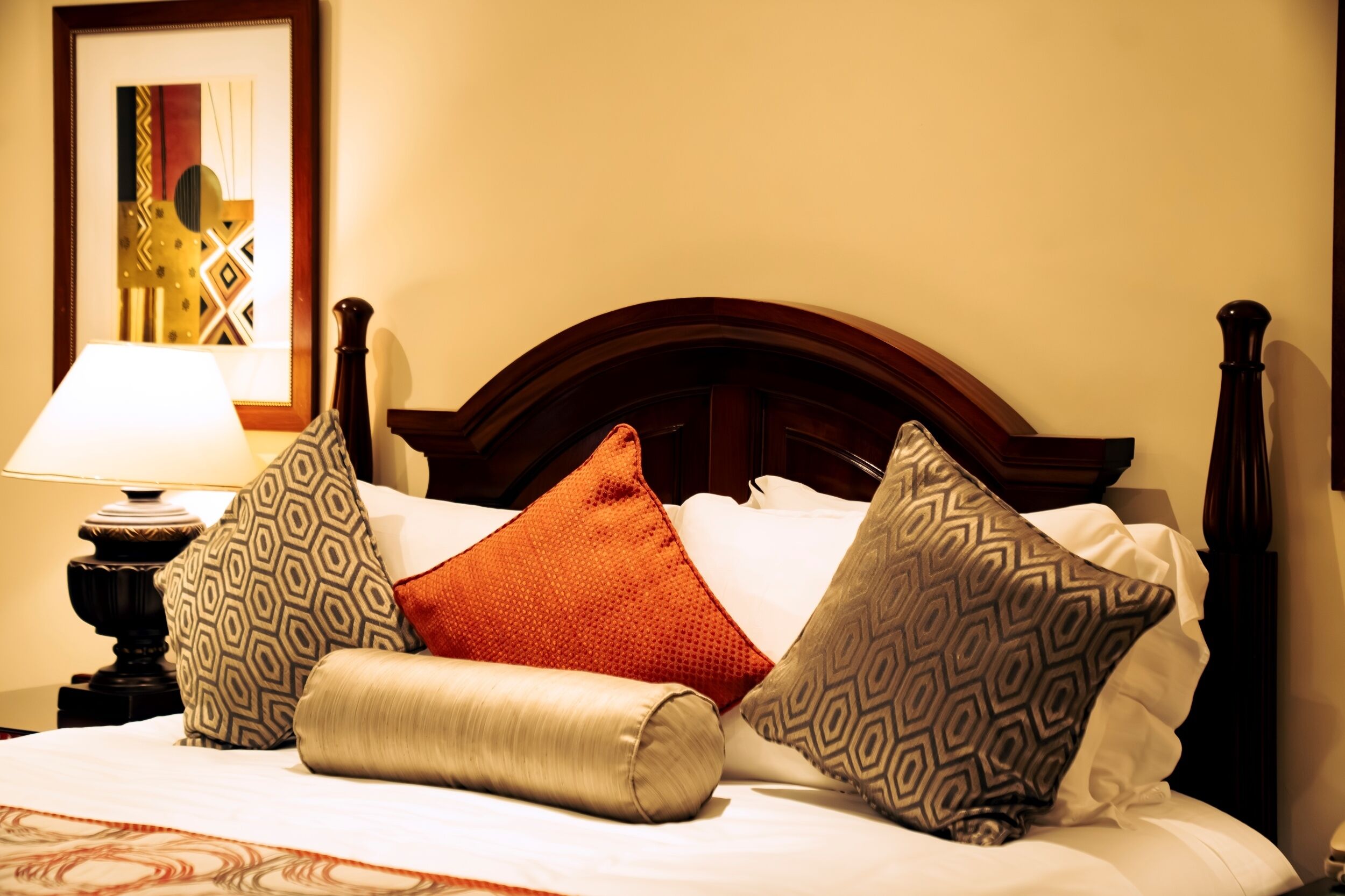 Une chambre d’hôtel avec une tête de lit en bois, un lit recouvert de draps blancs et plusieurs coussins à motifs.