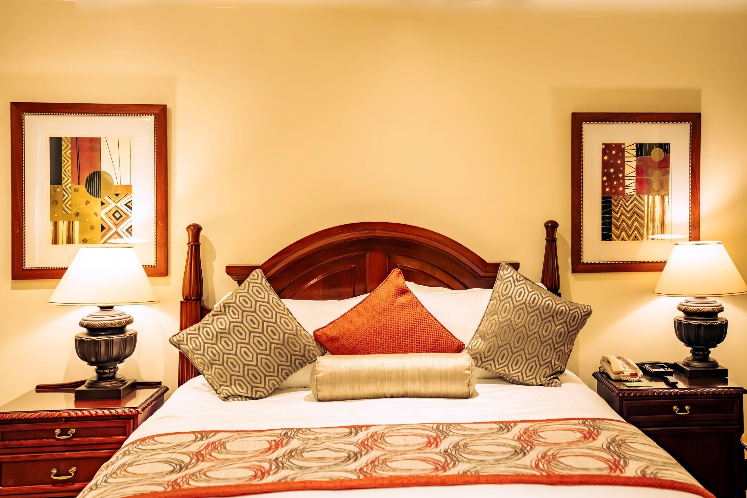 A hotel room with a wooden bed, two bedside lamps, a telephone, a nightstand, and a decorative wall hanging.