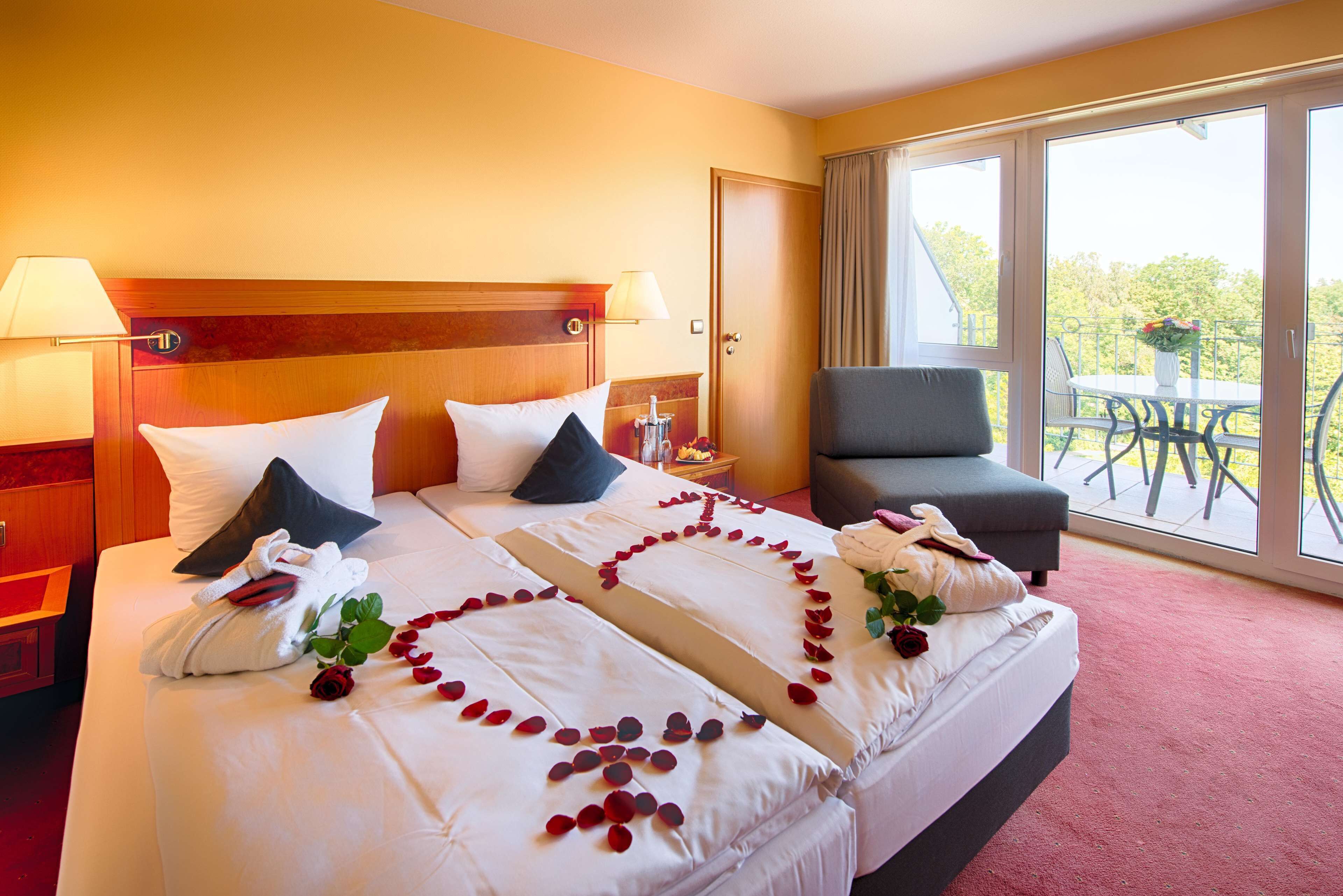 Ein Hotelzimmer mit einem großen Bett, einem Sessel und einem Balkon mit Tisch und Stühlen.