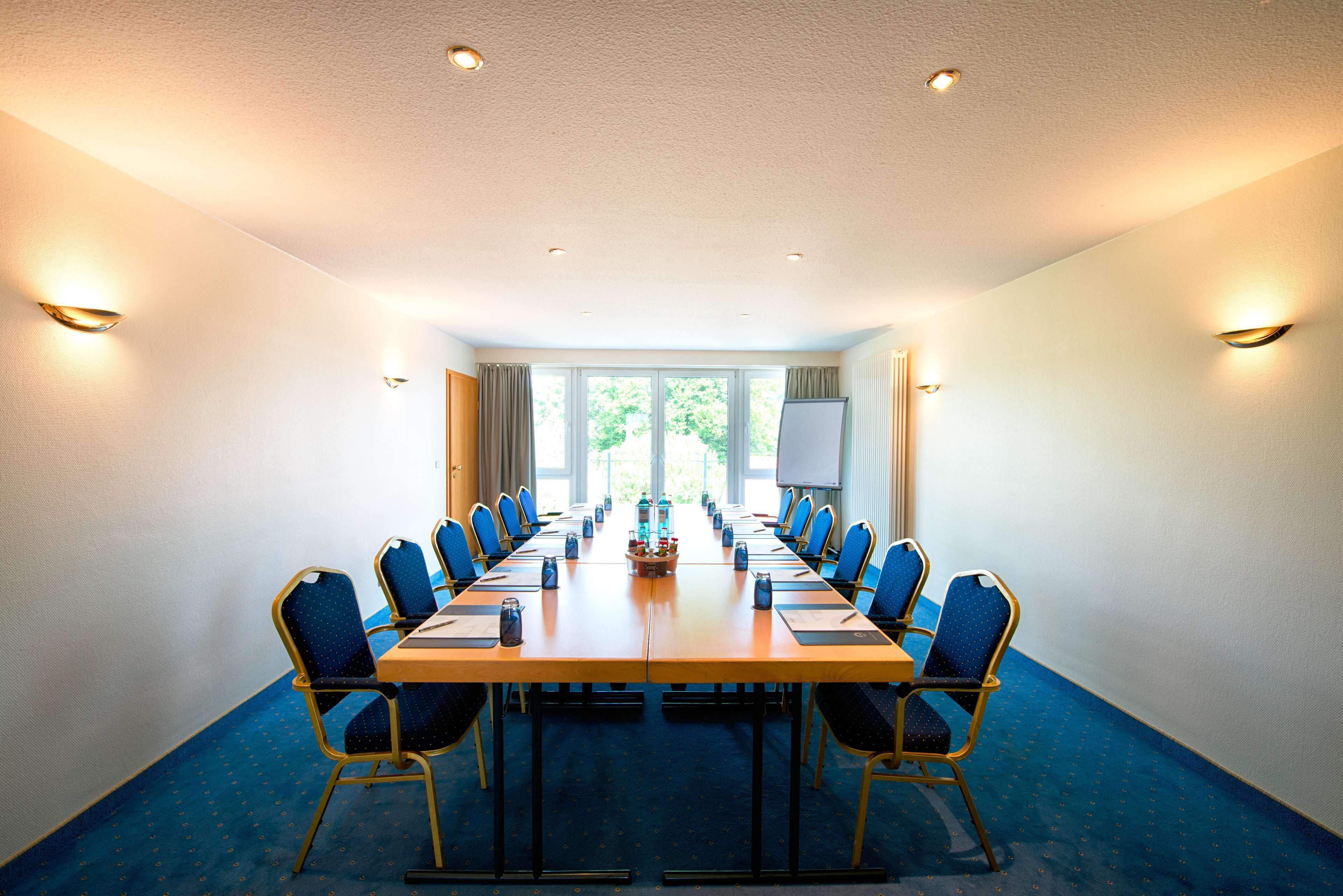 A conference room with a long table, blue chairs, and a projector screen.