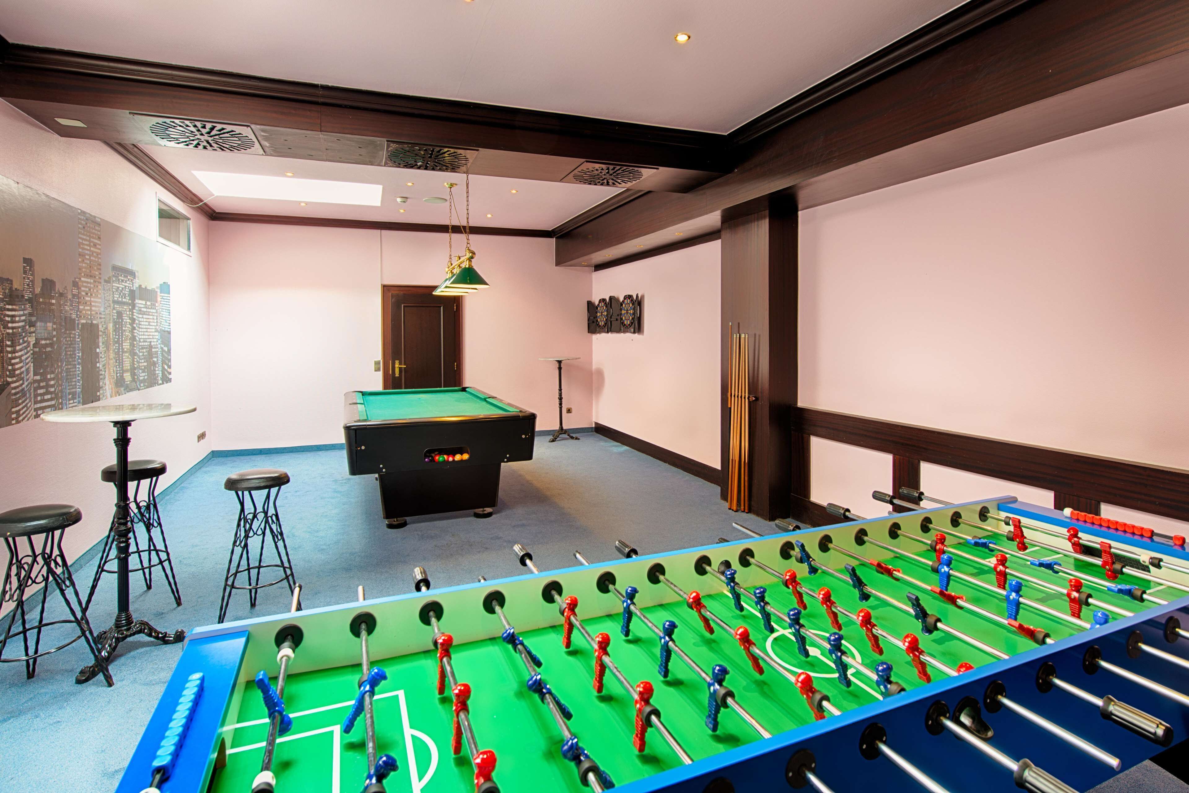 A room with a foosball table, a pool table, and a bar area with stools.