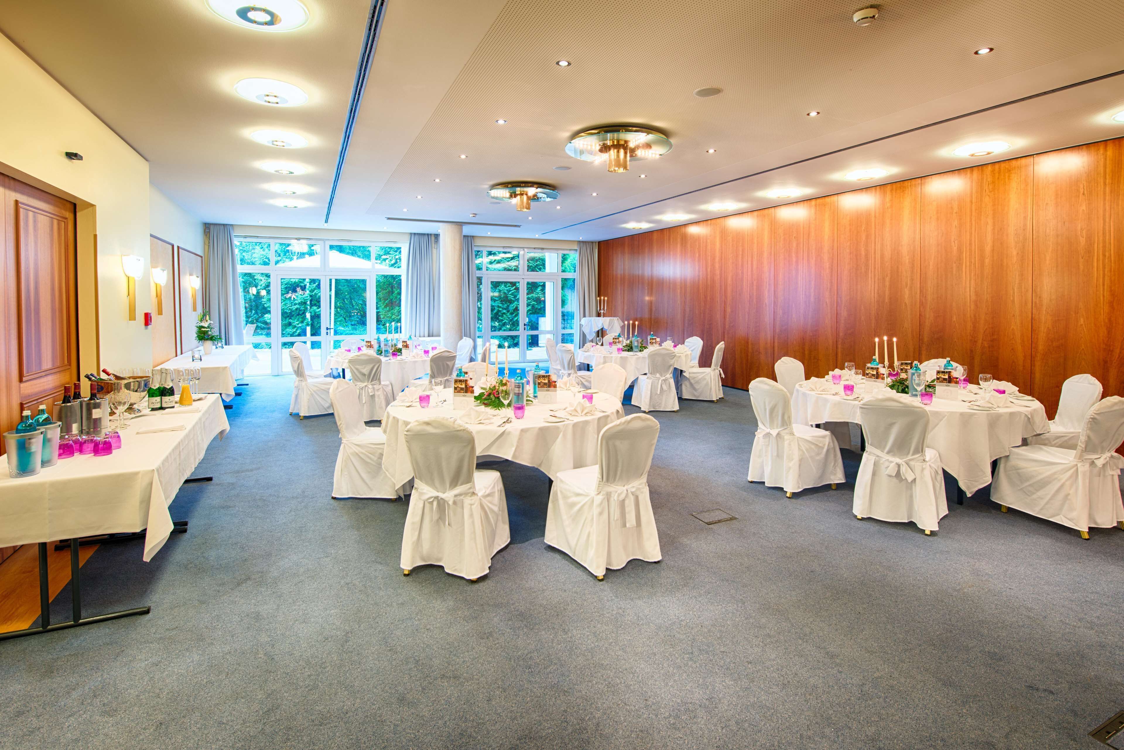 Un salón de banquetes con mesas redondas, sillas blancas y un muro de madera.