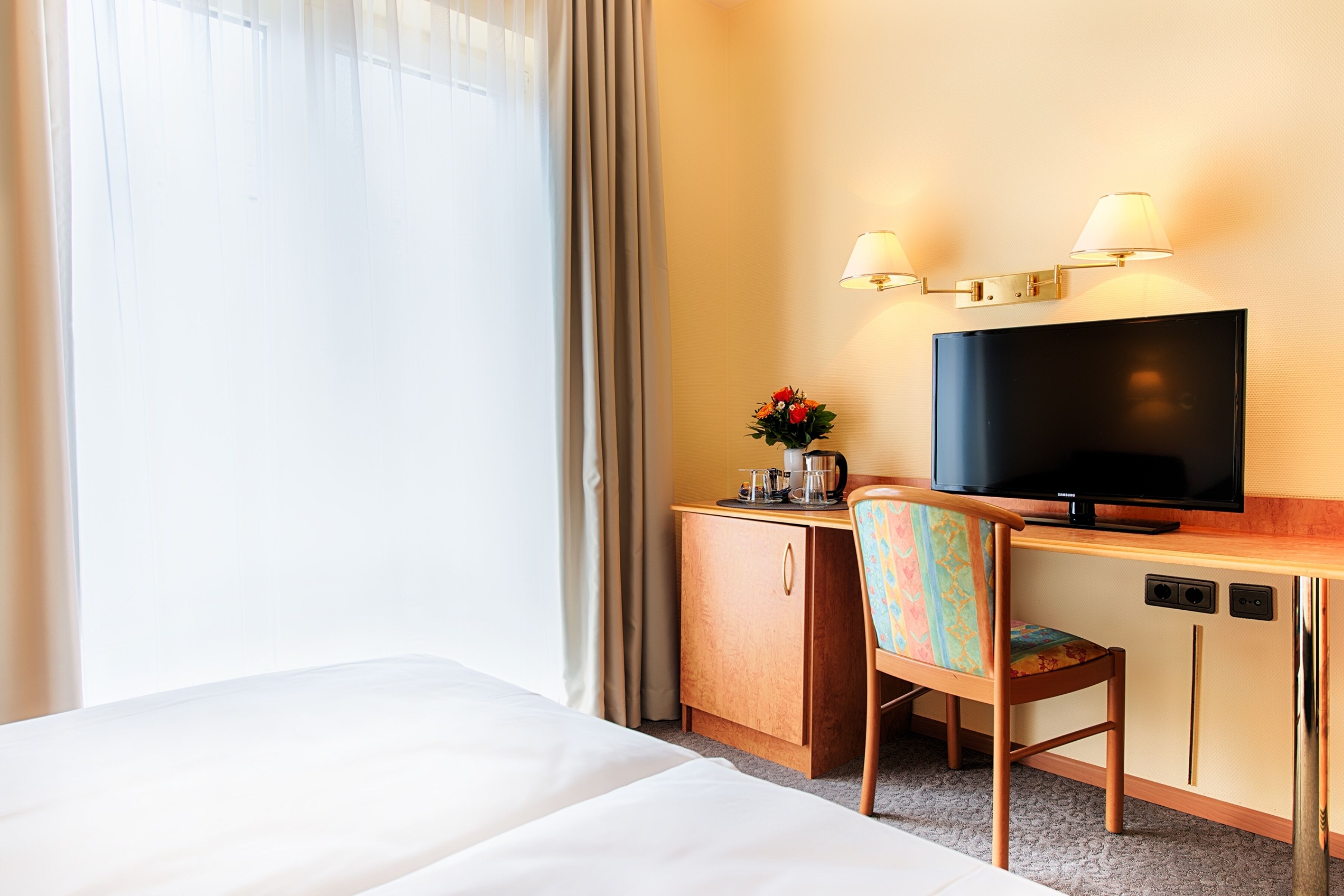 Una camera d'albergo con un letto, una scrivania con televisore, una sedia e un piccolo armadio.