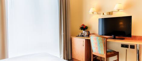 Una habitación de hotel con cama, escritorio con televisor, una silla y un pequeño armario.