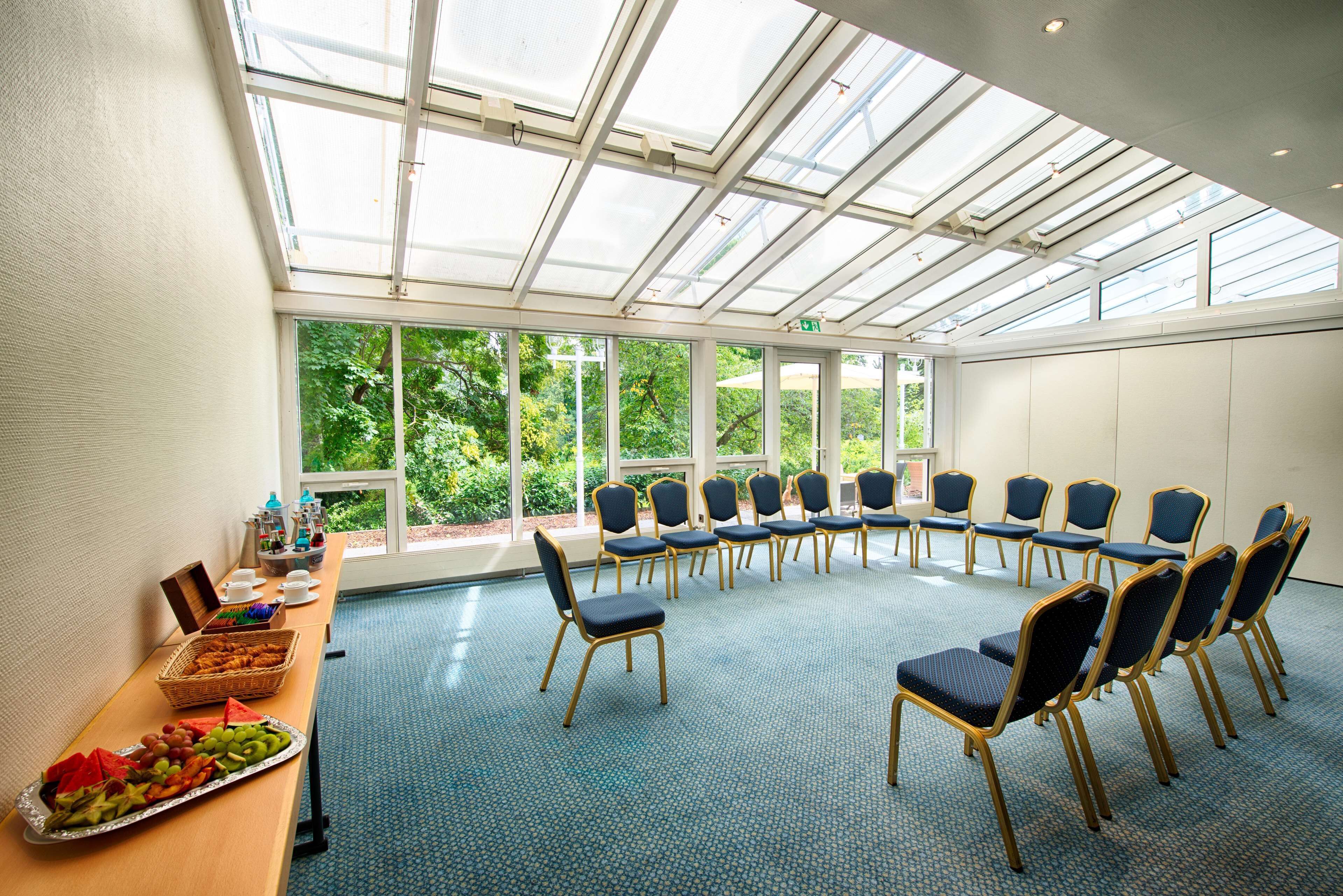 A conference room with a high ceiling and large windows, a buffet table with fruits and snacks, and rows of chairs arranged for a meeting.