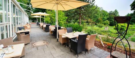 An outdoor patio area with tables and chairs, surrounded by greenery and trees.