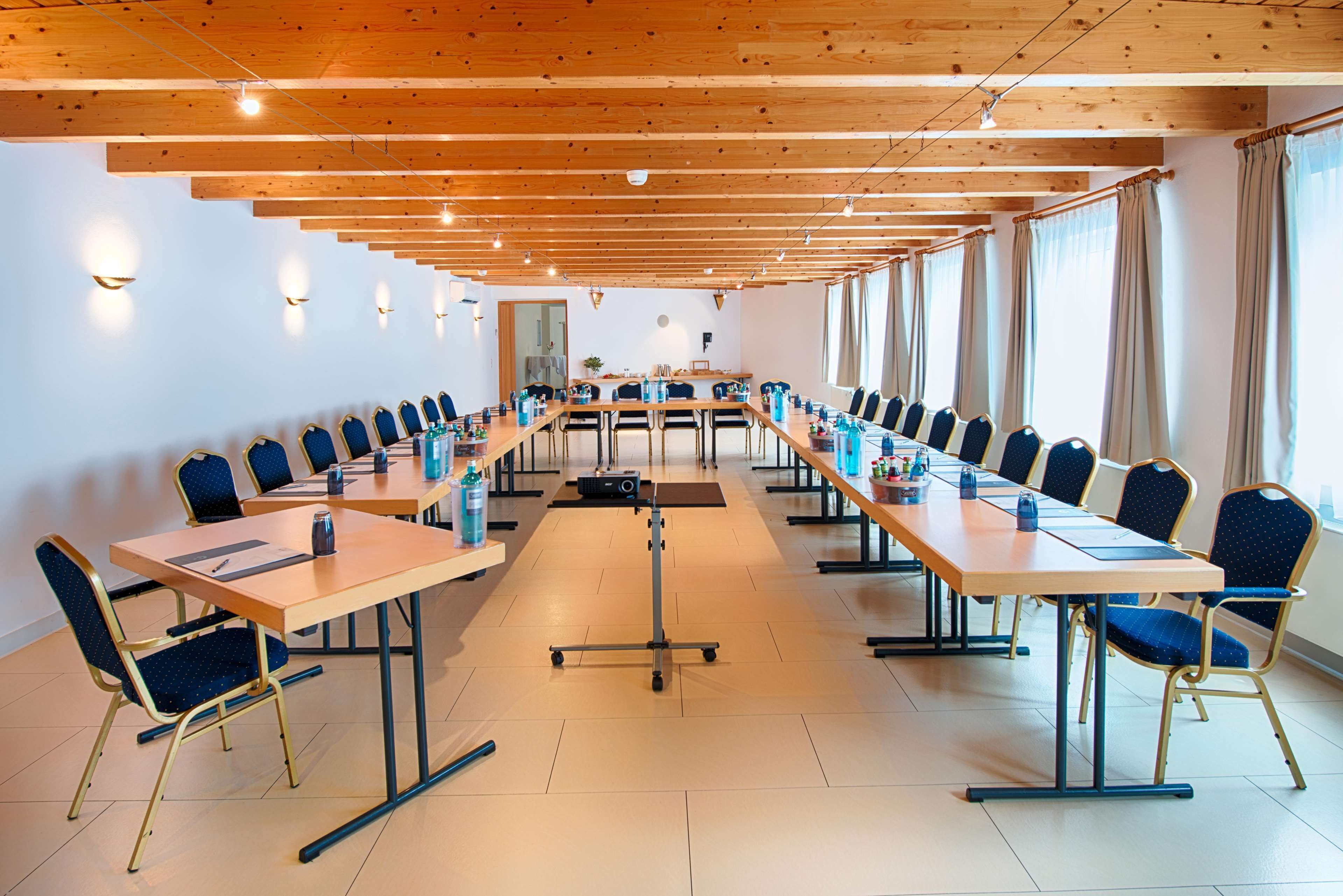 Kokoushuone, jossa on pitkiä pöytiä ja tuoleja, projektori ja valkotaulu.