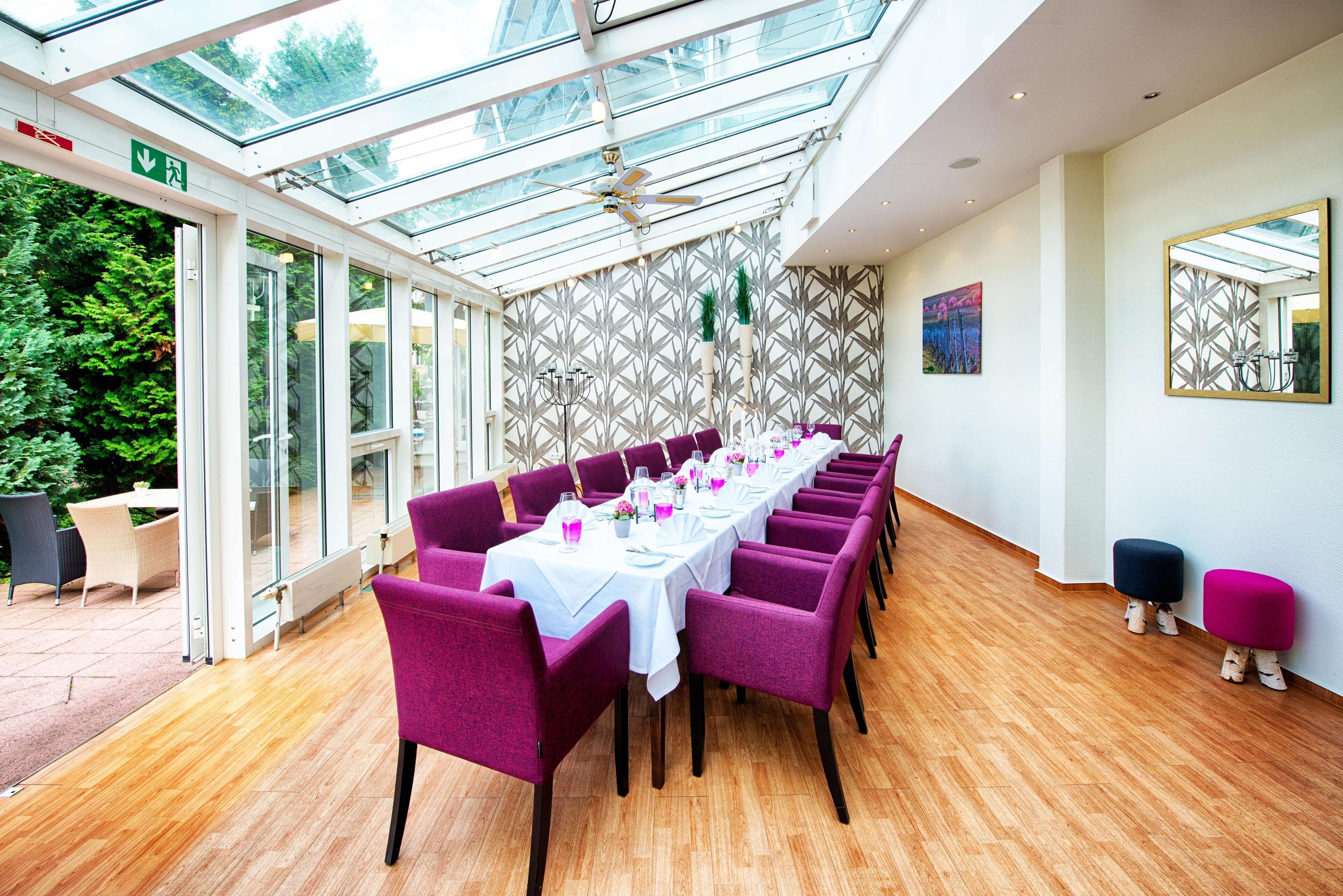 A long table with purple chairs and white tablecloths, a glass ceiling, and a patterned wall.