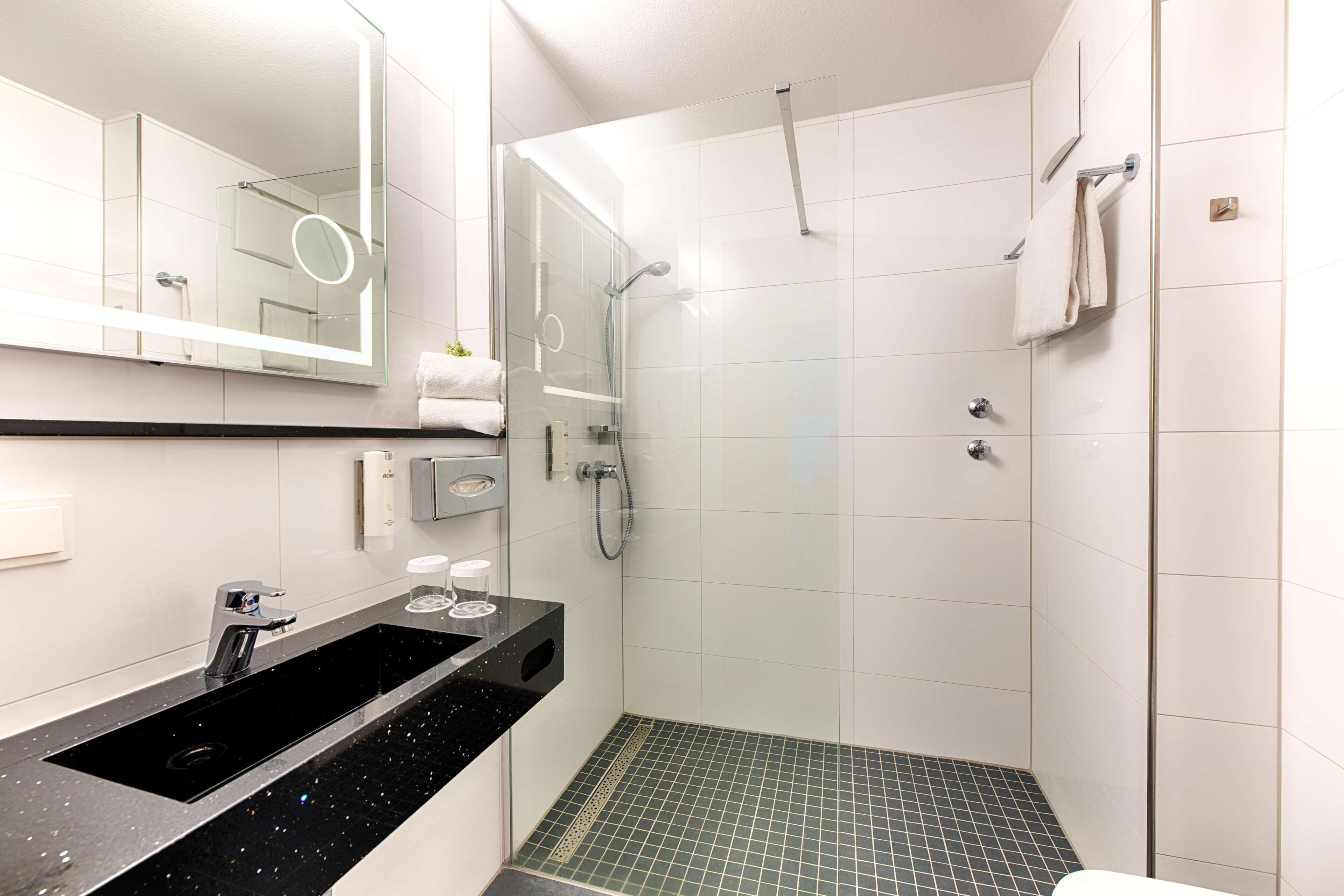 Ein modernes Badezimmer mit einem schwarzen Waschbecken, einer Duschkabine aus Glas und einem gefliesten Boden.