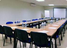Un salón de conferencias con una larga mesa, sillas azules, botellas de agua y una pizarra.