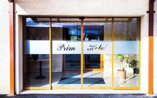 Entrada de un hotel con puerta de vidrio, un letrero que dice "Prim Hotel" y una planta en maceta afuera.