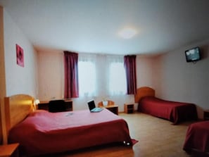 Habitación de hotel con dos camas, un escritorio con una computadora portátil, un televisor en la pared y una ventana con cortinas.