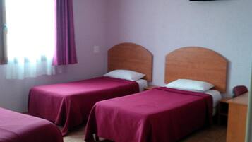 A hotel room with two single beds, a wooden headboard, a television on the wall, and a window with curtains.