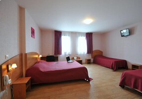 Una habitación de hotel con una cama individual, un escritorio con una computadora portátil, una mesita de noche, una silla y un televisor en la pared.
