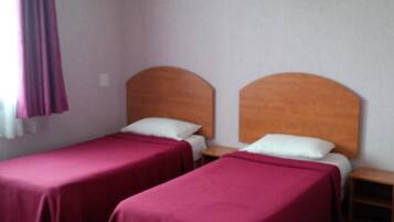 Una habitación con dos camas individuales, cada una con cabecero de madera, una mesita de noche pequeña y un televisor fijado a la pared.