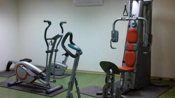 Un gimnasio con equipo de ejercicio, incluyendo cintas de correr y una máquina de pesas, sobre colchonetas verdes.